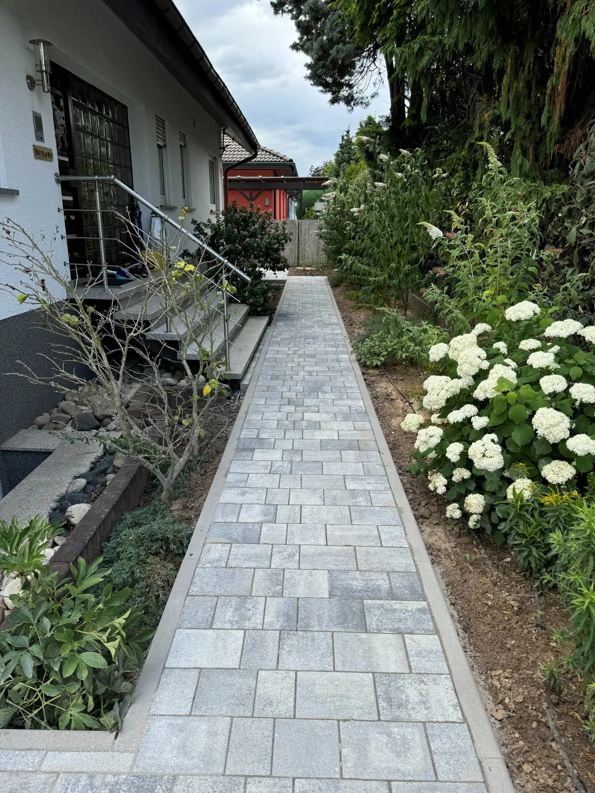 Schmaler Pflasterweg neben blühenden Beeten